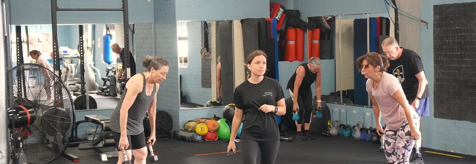 A coach taking two members through a strength set in the Solutions4Wellbeing gym